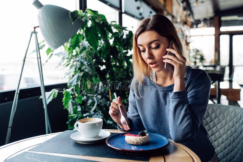 Attractive woman talking on mobile phone while eating at cafe. 