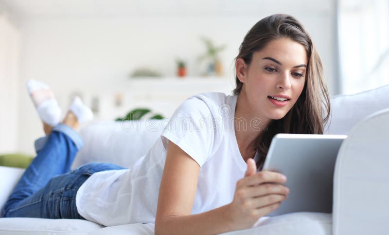 Beautiful young woman using tablet sitting on sofa at home at living room. royalty free stock photo