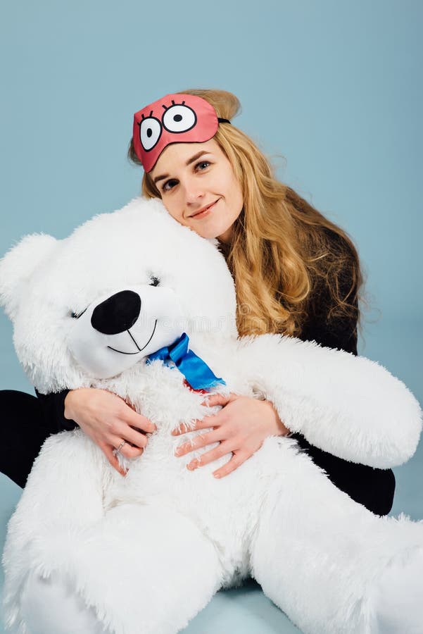 A beautiful young woman wearing pajamas hugging her stuffed teddy bear. 