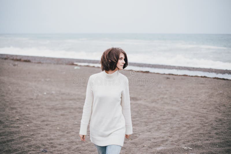 Beautiful young woman wearing white sweater and blue jeans walking on a lonely beach stock images Beautiful young woman wearing white sweater and blue jeans walking on a lonely beach stock images