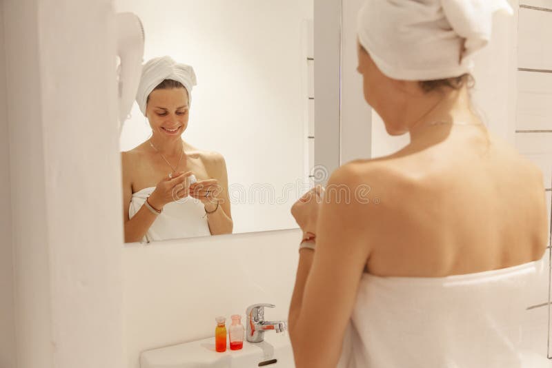 Beautiful young woman in a white towel in the bathroom in front of the mirror, use cosmetics. home care concept royalty free stock photo Beautiful young woman in a white towel in the bathroom in front of the mirror, use cosmetics. home care concept royalty free stock photo