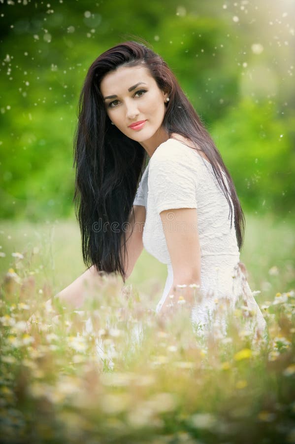 Beautiful young woman in wild flowers field.Portrait of attractive brunette girl with long hair relaxing in nature, outdoor shot