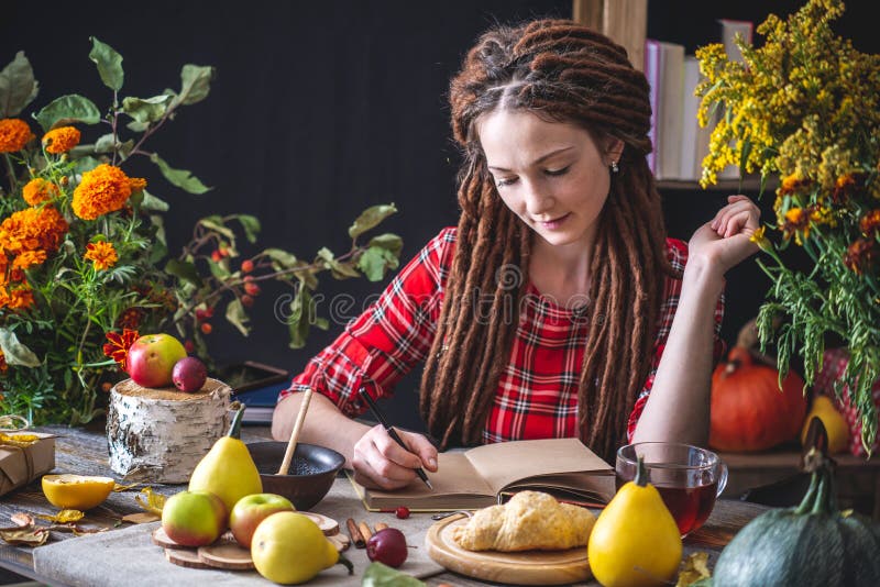 Beautiful young woman writes autumn dreams in a notebook. Fall table with flowers. Concept of autumn romantic mood