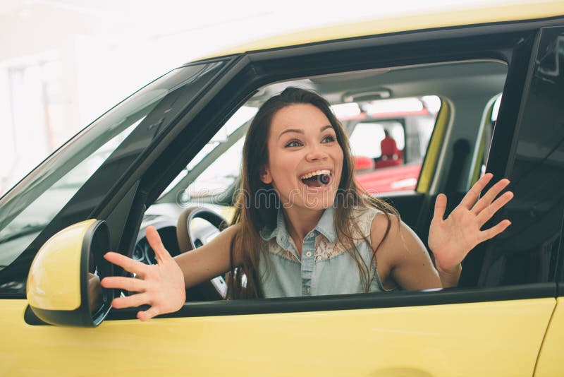 Beautiful young woman buying a car at dealership. Female model sitting Sits in the car interior