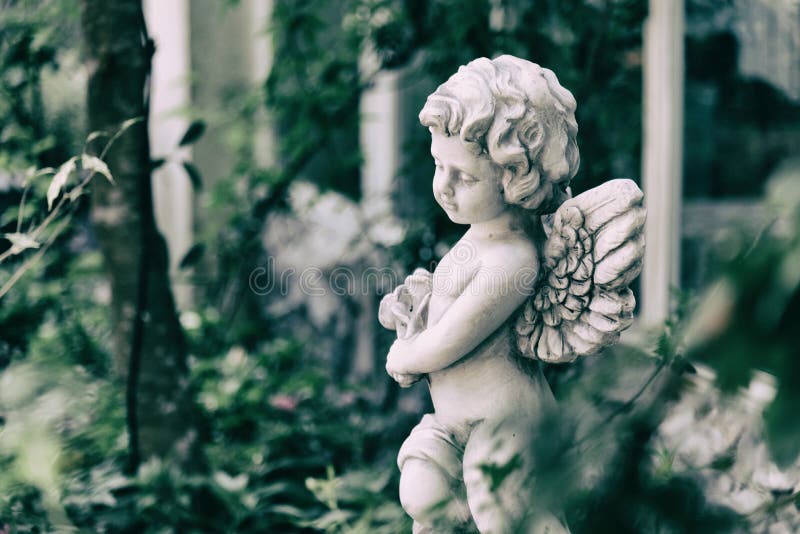 Beauty Cupid statue of Angel in vintage garden on summer. Holding bouquet flowers in his hand