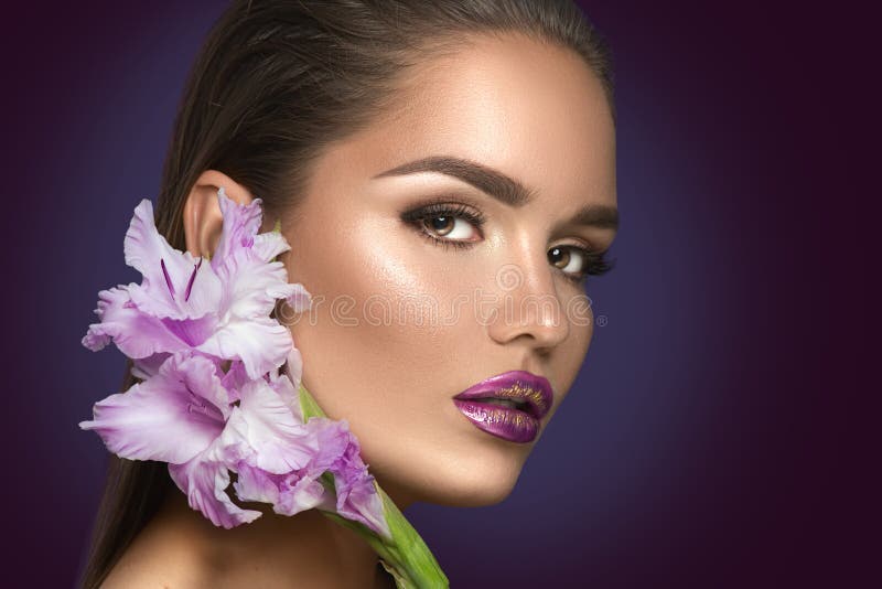 Beauty fashion brunette girl with gladiolus flowers. Glamour woman with perfect violet trendy makeup royalty free stock photo Beauty fashion brunette girl with gladiolus flowers. Glamour woman with perfect violet trendy makeup royalty free stock photo