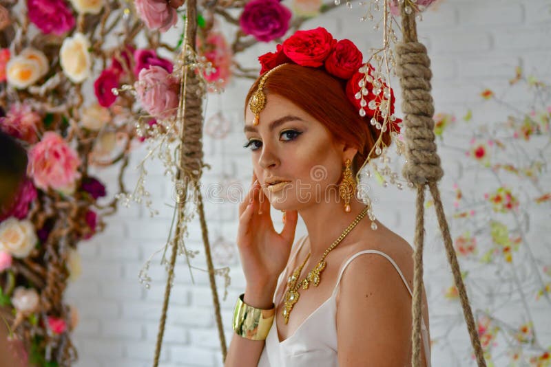 Beauty Girl With Flowers on a swing. Model Woman and red flowers on her head stock photo Beauty Girl With Flowers on a swing. Model Woman and red flowers on her head stock photo