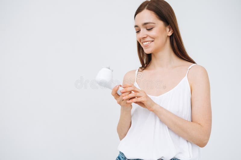 Beauty portrait of happy smiling woman with dark long hair with facial massager in hand on clean fresh skin face on white