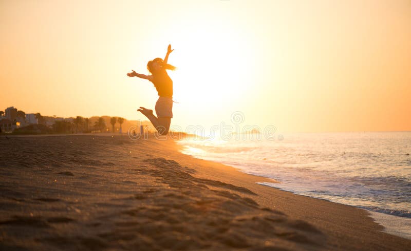 Beauty young happy woman jumping, sea side. Girl\'s silhouette on a summer beach over sunrise