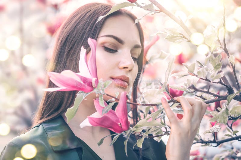 Beauty young woman enjoying nature in spring spring magnolia flowers. Beautiful brunette girl in Garden with blooming magnolias