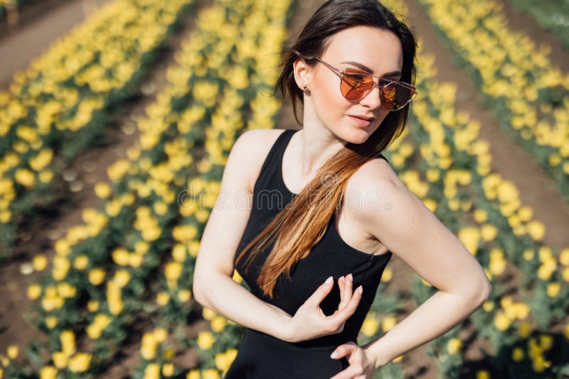 Beauty young woman in sunglasses in black dress in tulips field garden