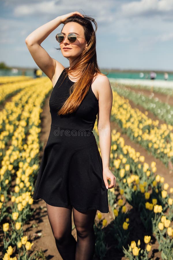 Beauty young woman in sunglasses in black dress in tulips field garden