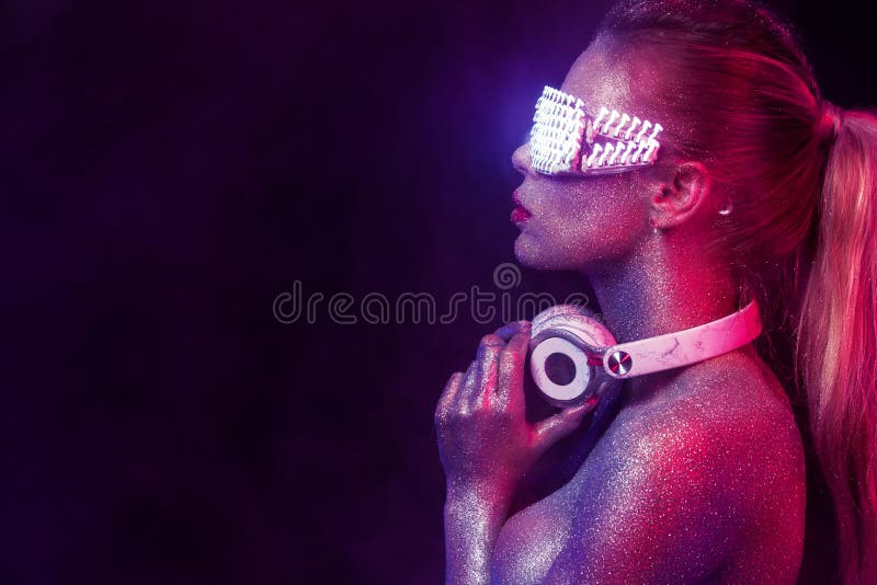Beautyful girl with glitter and sparkles on her face and body. Portrait of TDJ with headphones and neon sunglasses