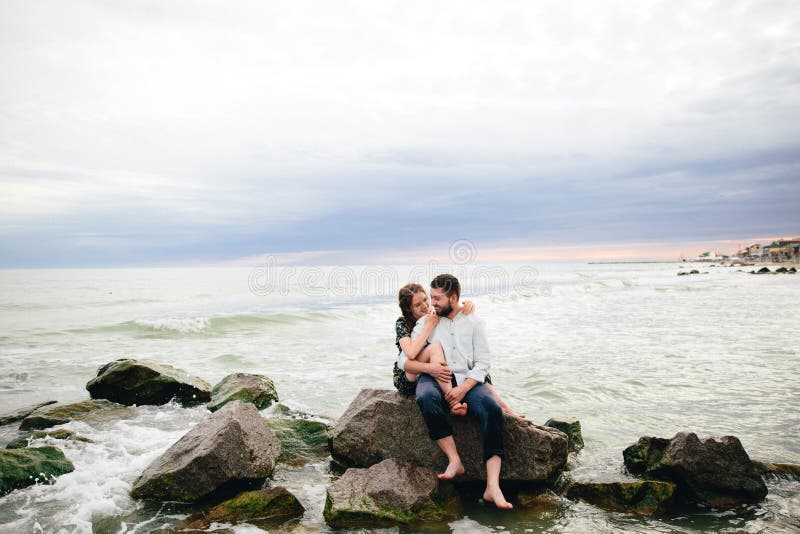 Beaux couples dans l'amour étreignant sur la plage Se reposer sur les roches photographie stock Beaux couples dans l'amour étreignant sur la plage Se reposer sur les roches photographie stock