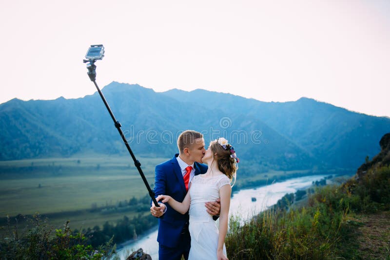 Beaux jeunes couples les ?pousant faisant le selfie sur le fond des montagnes et de la rivi?re photographie stock Beaux jeunes couples les ?pousant faisant le selfie sur le fond des montagnes et de la rivi?re photographie stock