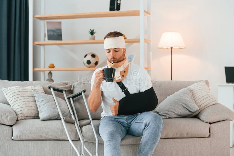 Beber de la taza. el hombre con muletas está en casa. lesiones imagen de archivo