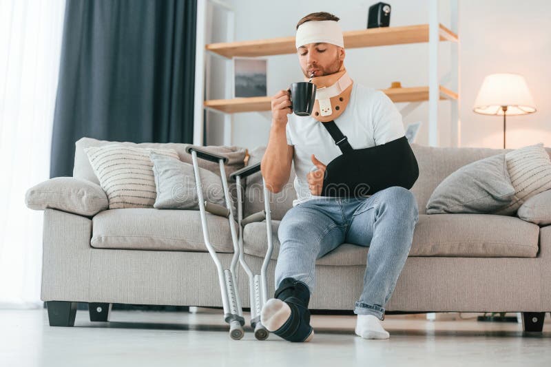 Beber de la taza. el hombre con muletas está en casa. lesiones imagen de archivo