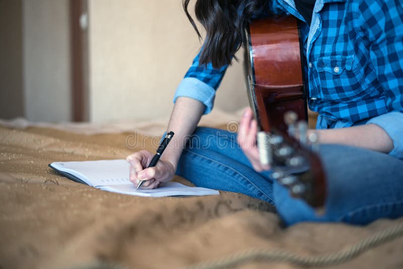Bebouwd beeld van vrouwelijke handen die in een notitieboekje met een akoestische gitaar schrijven stock afbeeldingen Bebouwd beeld van vrouwelijke handen die in een notitieboekje met een akoestische gitaar schrijven stock afbeeldingen