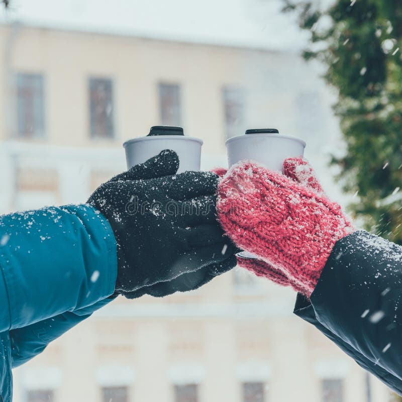 cropped shot of couple holding thermocups with hot drinks on street in winter. cropped shot of couple holding thermocups with hot drinks on street in winter