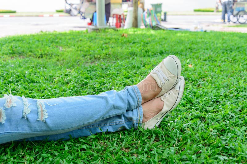 Bebouwde vrouwenbenen in denim met witte tennisschoenen die op gras rusten stock foto's Bebouwde vrouwenbenen in denim met witte tennisschoenen die op gras rusten stock foto's
