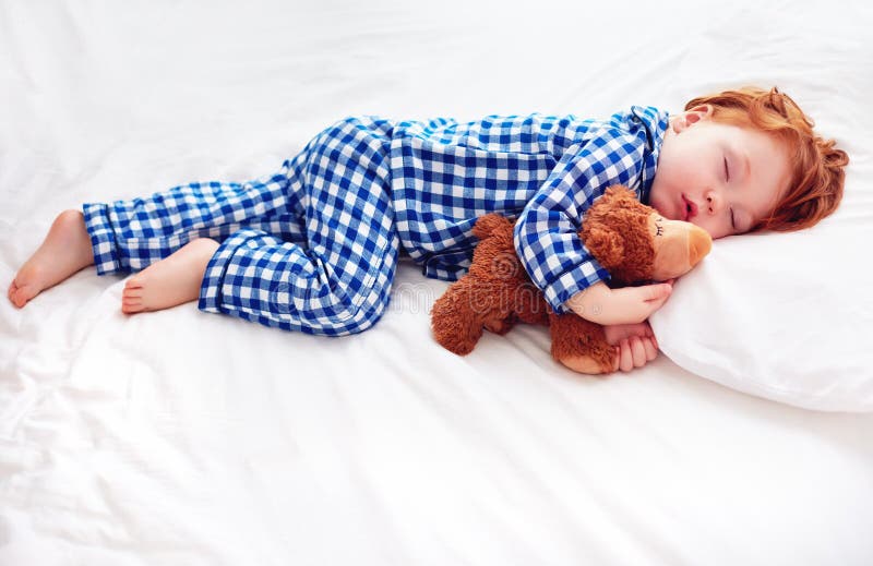 Bebé adorable del niño del pelirrojo en pijamas de la franela que duerme con el juguete del calentador de la felpa foto de archivo libre de regalías Bebé adorable del niño del pelirrojo en pijamas de la franela que duerme con el juguete del calentador de la felpa foto de archivo libre de regalías