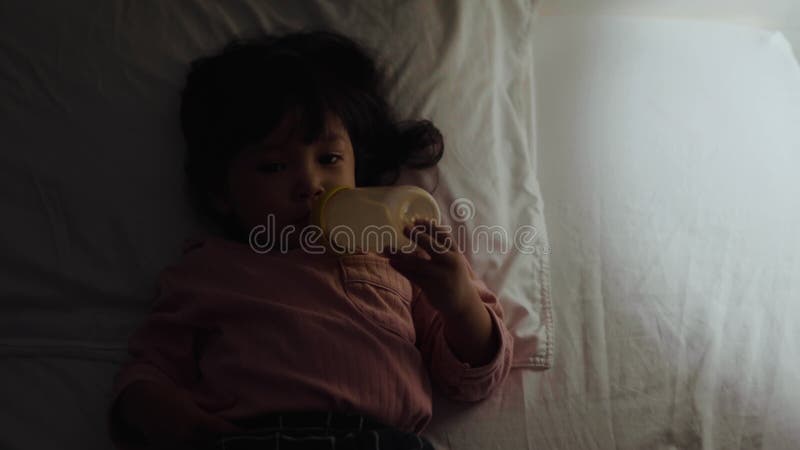Bebé bebe leche de una botella en la cama por la noche metrajes