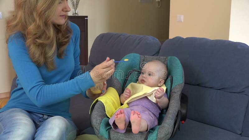 Bebé cariñoso de la hija de la alimentación de la madre con la cuchara en casa 4K