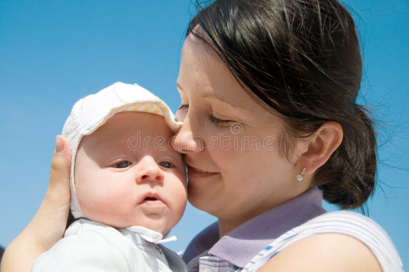 Baby in mother's arms on blue sky background. Baby in mother's arms on blue sky background