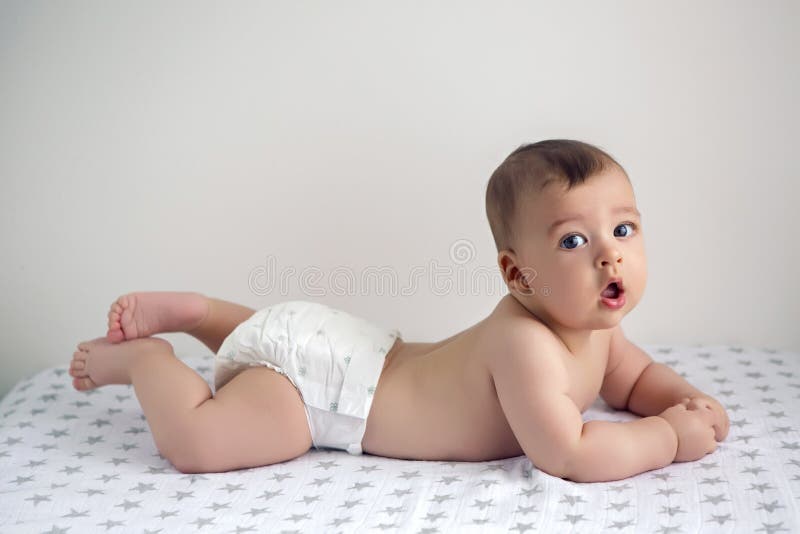 Bebé desnudo en los pañales que mienten en su vientre fotografía de archivo Bebé desnudo en los pañales que mienten en su vientre fotografía de archivo