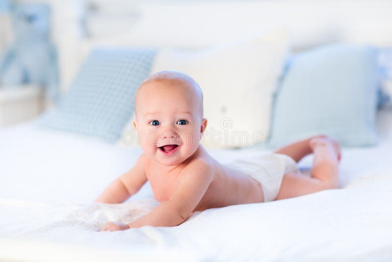 Baby boy wearing diaper in white sunny bedroom. Newborn child relaxing in bed. Nursery for children. Textile and bedding for kids. Family morning at home. New born kid during tummy time with toy bear. Baby boy wearing diaper in white sunny bedroom. Newborn child relaxing in bed. Nursery for children. Textile and bedding for kids. Family morning at home. New born kid during tummy time with toy bear.