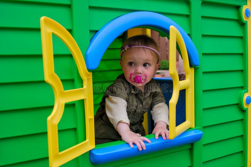 Little girl with soother looking out of window of a green playhouse. Little girl with soother looking out of window of a green playhouse