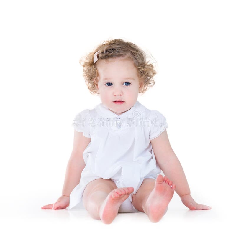 Bebé hermoso con el pelo rizado en vestido blanco agradable fotos de archivo Bebé hermoso con el pelo rizado en vestido blanco agradable fotos de archivo