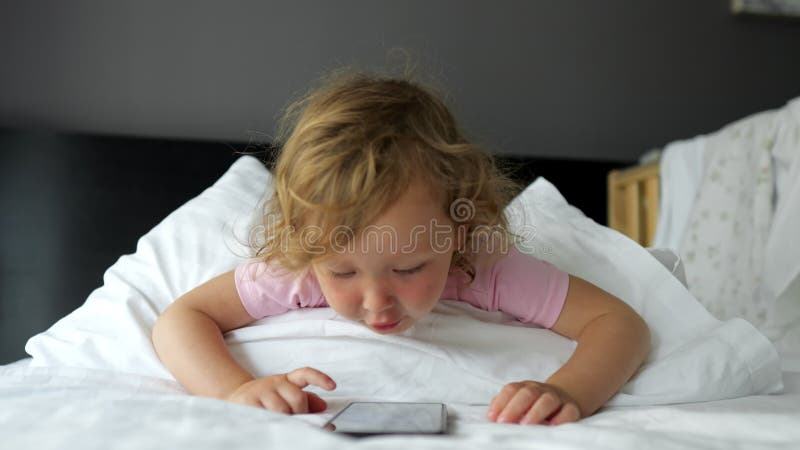 Bebé jugando con un smartphone en la cama almacen de video