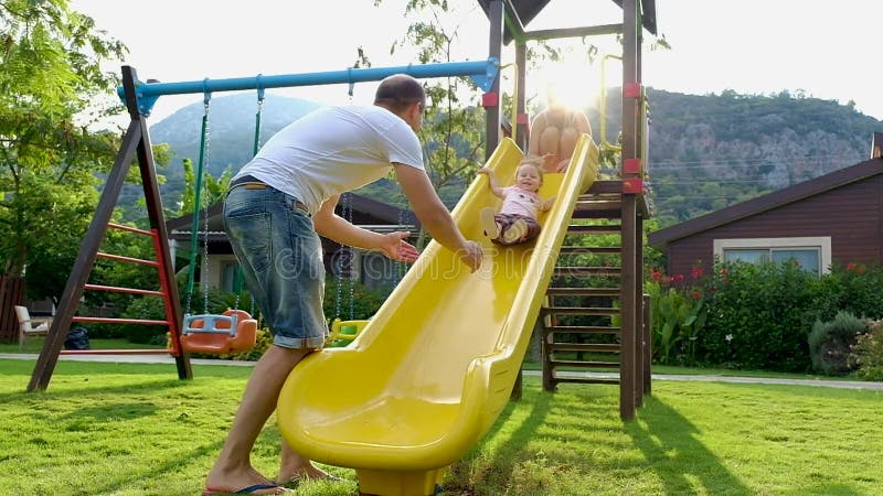 Bebé lindo divertido con sus padres que juegan en diapositiva del patio almacen de metraje de vídeo