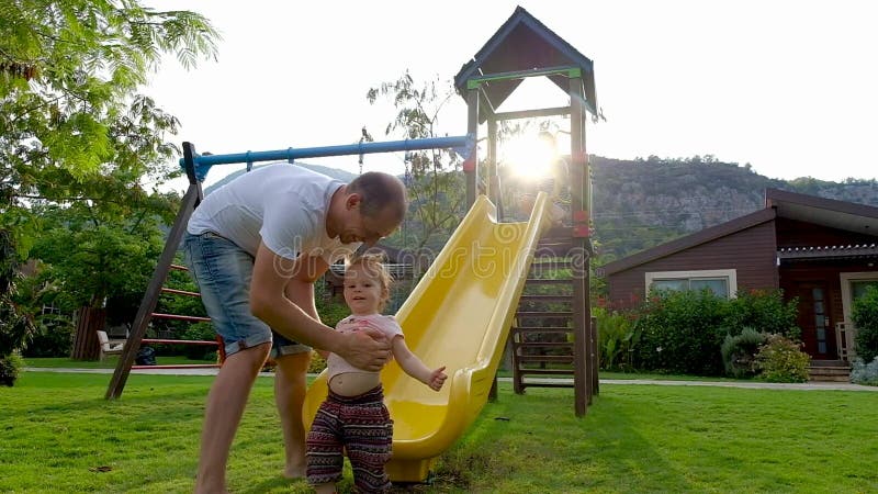Bebé lindo divertido con sus padres que juegan en diapositiva del patio metrajes