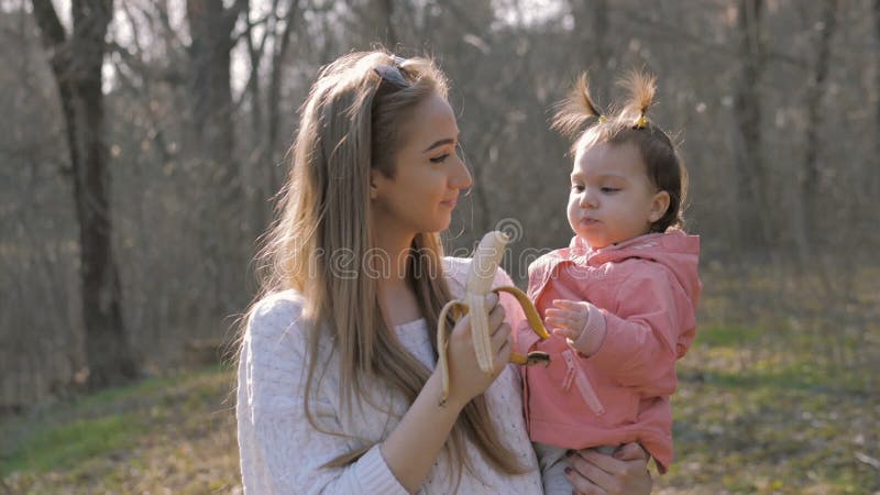 Bebé lindo que come el plátano en los brazos de la madre