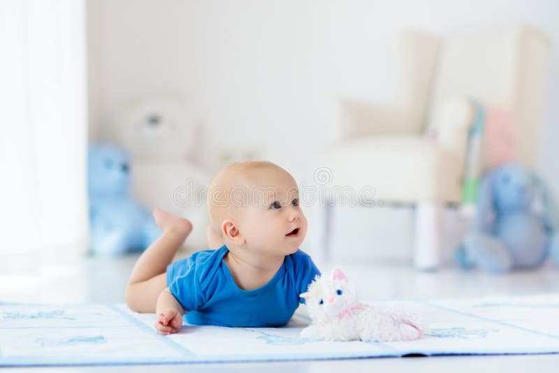 Adorable baby boy learning to crawl and playing with colorful toy in white sunny bedroom. Cute laughing child crawling on a play mat. Nursery interior, clothing and toys for little kids. Adorable baby boy learning to crawl and playing with colorful toy in white sunny bedroom. Cute laughing child crawling on a play mat. Nursery interior, clothing and toys for little kids.