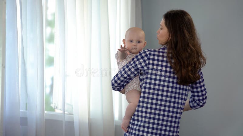 Bebé que mira en la cámara y la mano que agita, madre cariñosa que conforta al niño foto de archivo Bebé que mira en la cámara y la mano que agita, madre cariñosa que conforta al niño foto de archivo