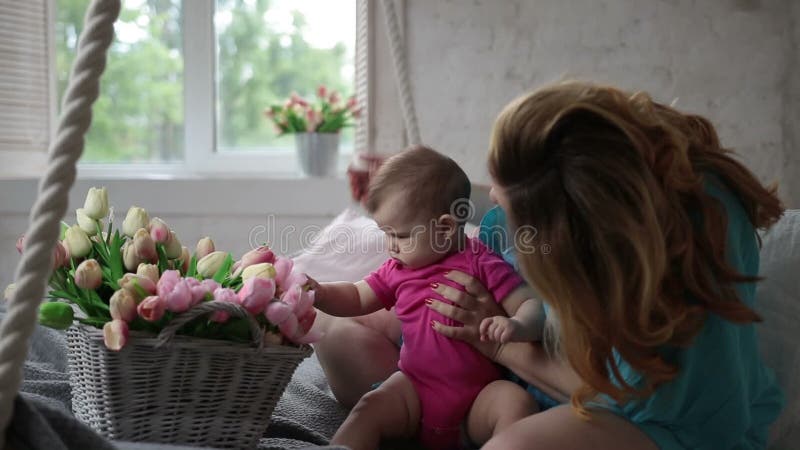 Bebê adorável que joga com flores da tulipa