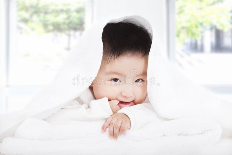 Bebê asiático que suga o dedo sob a cobertura ou a toalha