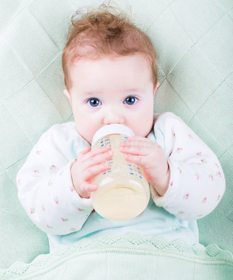 Bebê bonito com uma garrafa de leite sob uma cobertura feita malha morna fotografia de stock Bebê bonito com uma garrafa de leite sob uma cobertura feita malha morna fotografia de stock