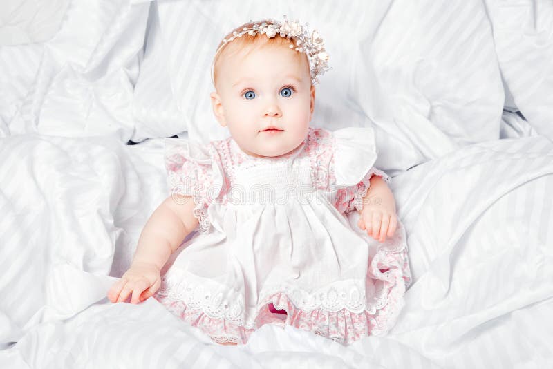 Bebê bonito e consideravelmente novo no vestido agradável sobre a cobertura branca imagem de stock royalty free Bebê bonito e consideravelmente novo no vestido agradável sobre a cobertura branca imagem de stock royalty free