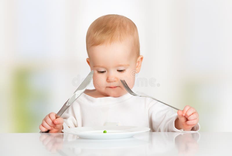 Bebê com comer da forquilha e da faca, olhando a placa com um p fotografia de stock Bebê com comer da forquilha e da faca, olhando a placa com um p fotografia de stock