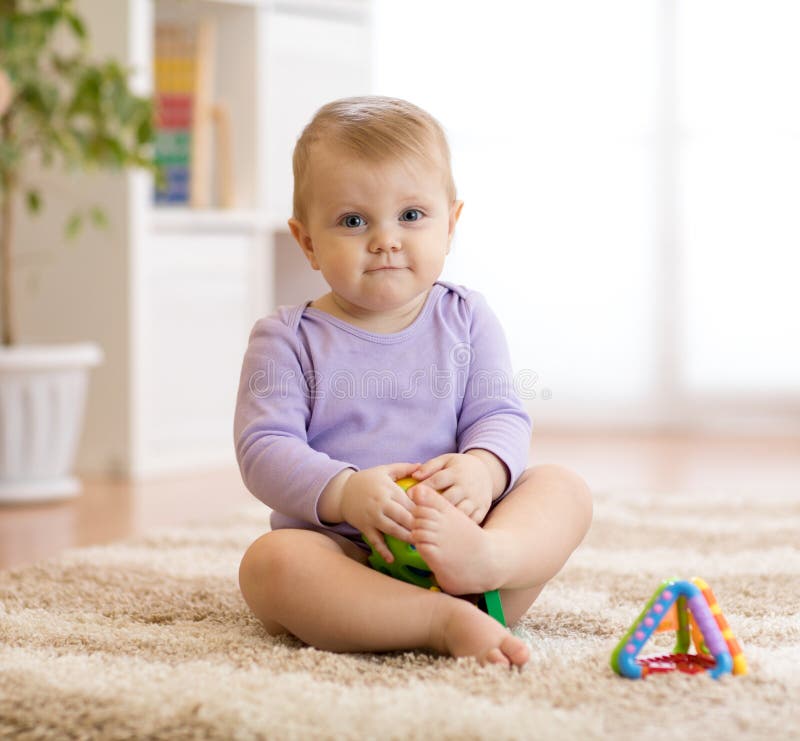 Bebê engraçado bonito que senta-se no tapete em casa foto de stock Bebê engraçado bonito que senta-se no tapete em casa foto de stock