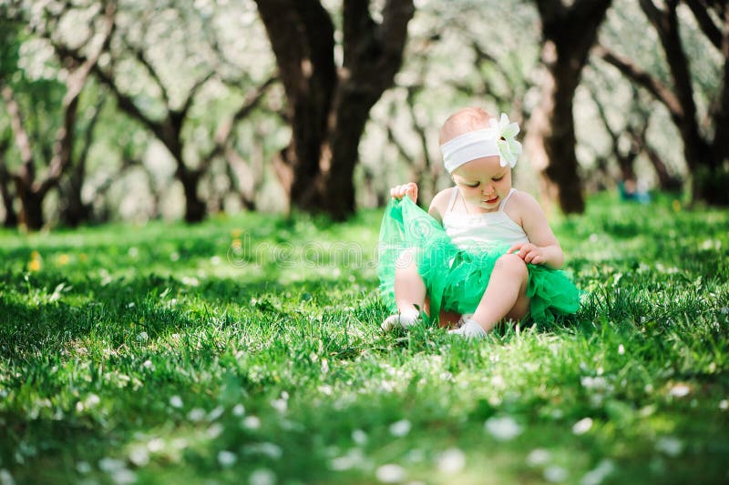 Bebê feliz bonito no passeio verde da saia do tutu exterior no jardim da mola imagem de stock royalty free Bebê feliz bonito no passeio verde da saia do tutu exterior no jardim da mola imagem de stock royalty free