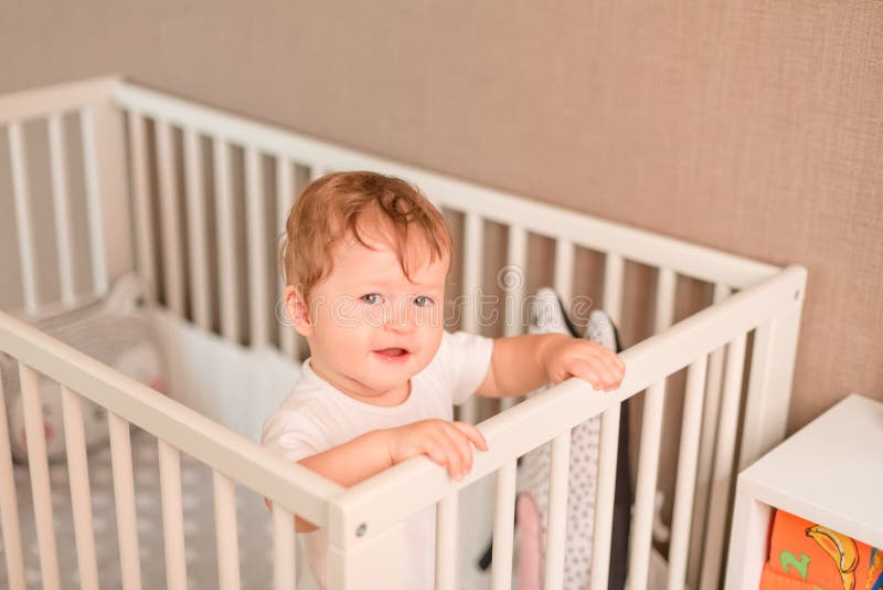 Bebê pequeno bonito que olha fora de sua cama imagem de stock Bebê pequeno bonito que olha fora de sua cama imagem de stock