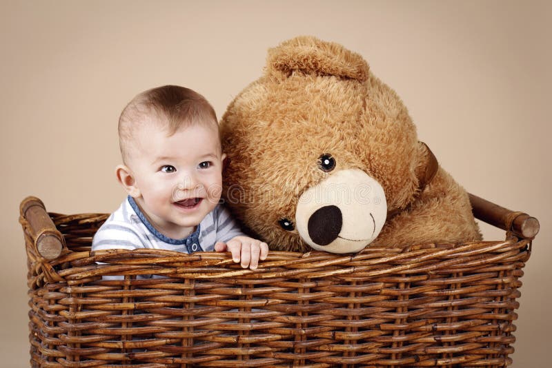 Bebê pequeno bonito que senta-se na cesta de vime com o urso de peluche grande do luxuoso foto de stock royalty free Bebê pequeno bonito que senta-se na cesta de vime com o urso de peluche grande do luxuoso foto de stock royalty free
