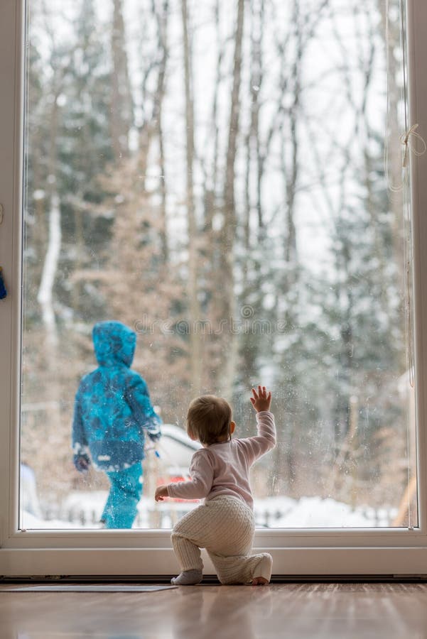 Bebê pequeno que olha um irmão jogar na neve imagens de stock Bebê pequeno que olha um irmão jogar na neve imagens de stock
