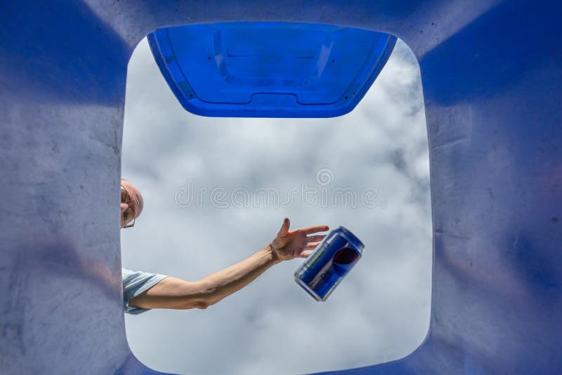 Man dropping soft drink can into blue recycling wheelie bin