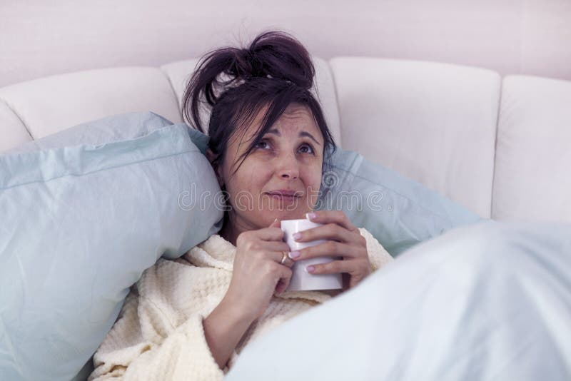 Bed rest at home. Brunette girl with a mug of tea in bed, dreams of recovery